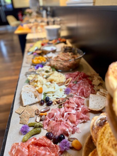 Bunte Auswahl an Wurst, Käse, Crackern und frischen Garnierungen auf einem Tisch.