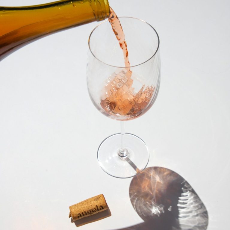 Roséwein wird aus einer Flasche in ein Glas gegossen, Korken daneben.