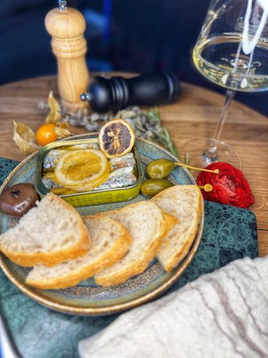 Ein Teller mit Brot, Käse, Oliven, einer Weintraube und einem Glas Weißwein.