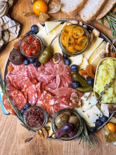 Ein rustikales Brett mit Wurst, Käse, Oliven, eingelegtem Gemüse und frischem Brot.