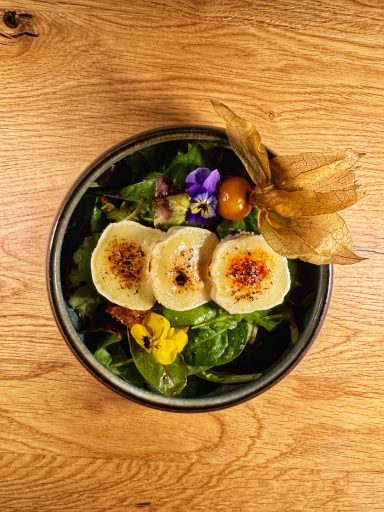 Salat mit gratiniertem Ziegenkäse, essbaren Blüten und Früchten.