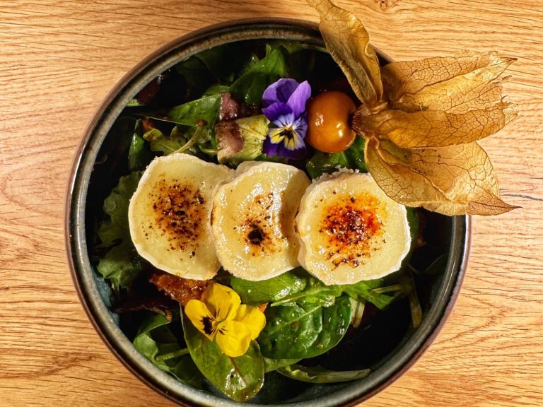 Salat mit essbaren Blumen und gegrillten Ziegenkäse in einer Schüssel.