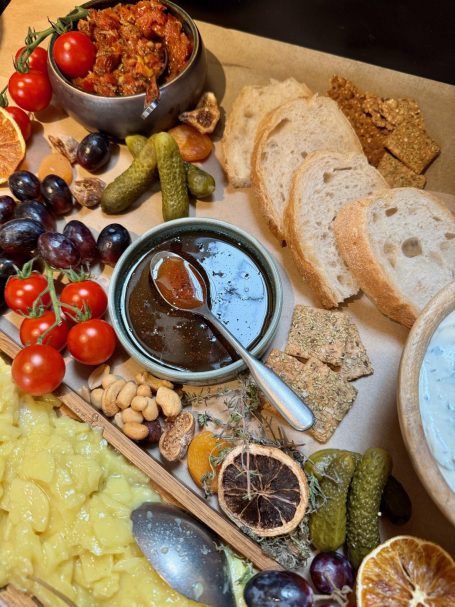 Ein rustikales Brett mit Brot, Oliven, Trauben, Nüssen, Dips und Trockenfrüchten.