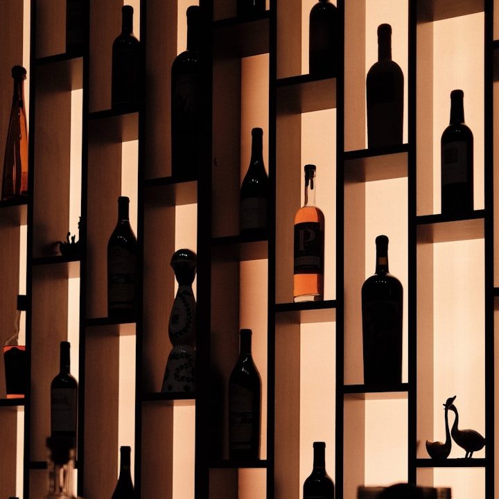 Regalwand mit verschiedenen Flaschen in Silhouette vor einem sanft beleuchteten Hintergrund.