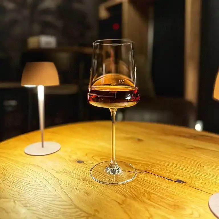 Ein Weinglas mit weißem Wein auf einem Holztisch, umgeben von kleinen Lampen.