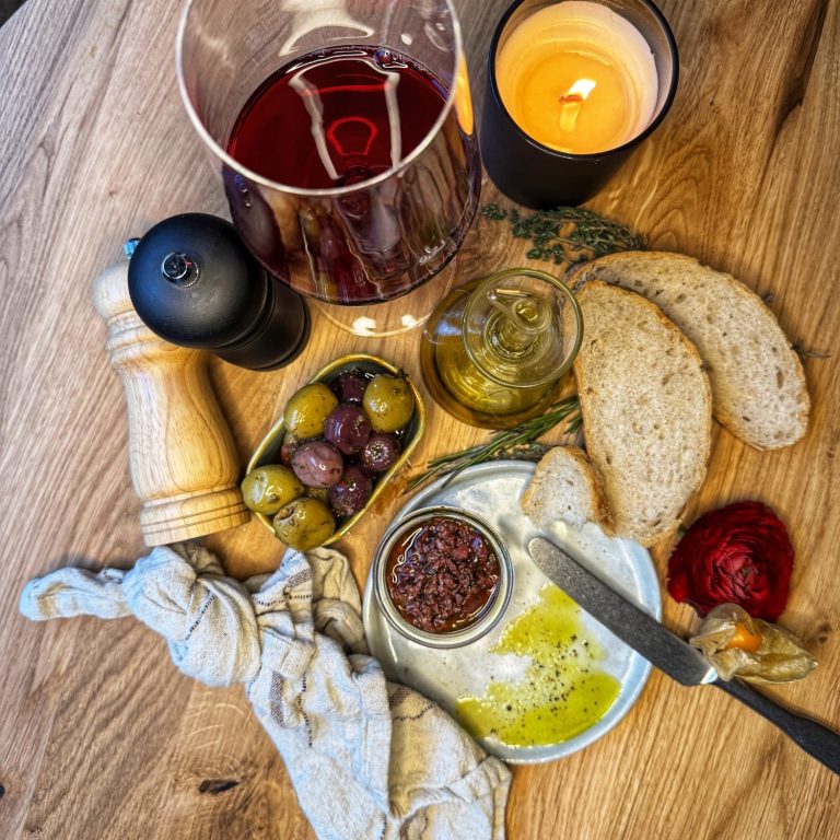 Ein rustikaler Tisch mit Brot, Oliven, Aufstrich, Öl und Kerzenlicht.