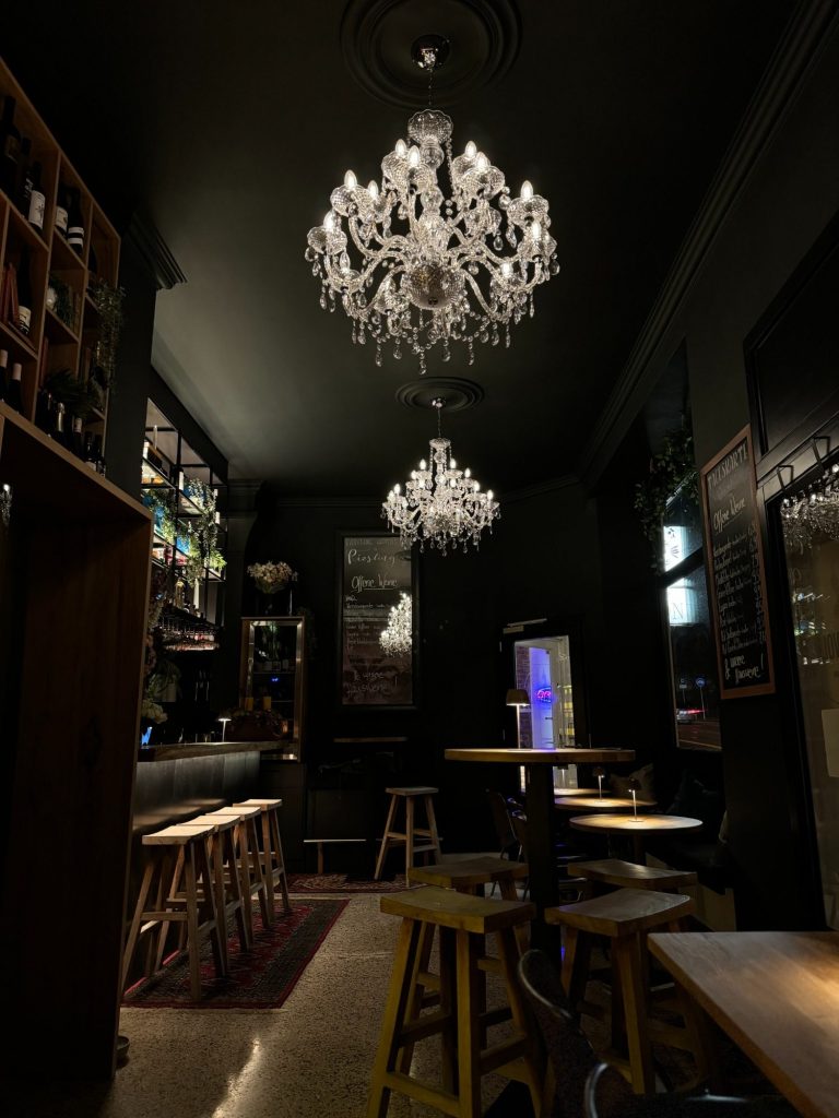 Elegante Bar Halbvoll in Kassel mit zwei Kristalllüstern und Holzinterieur in gedämpfter Beleuchtung, ideal zum Wein trinken.