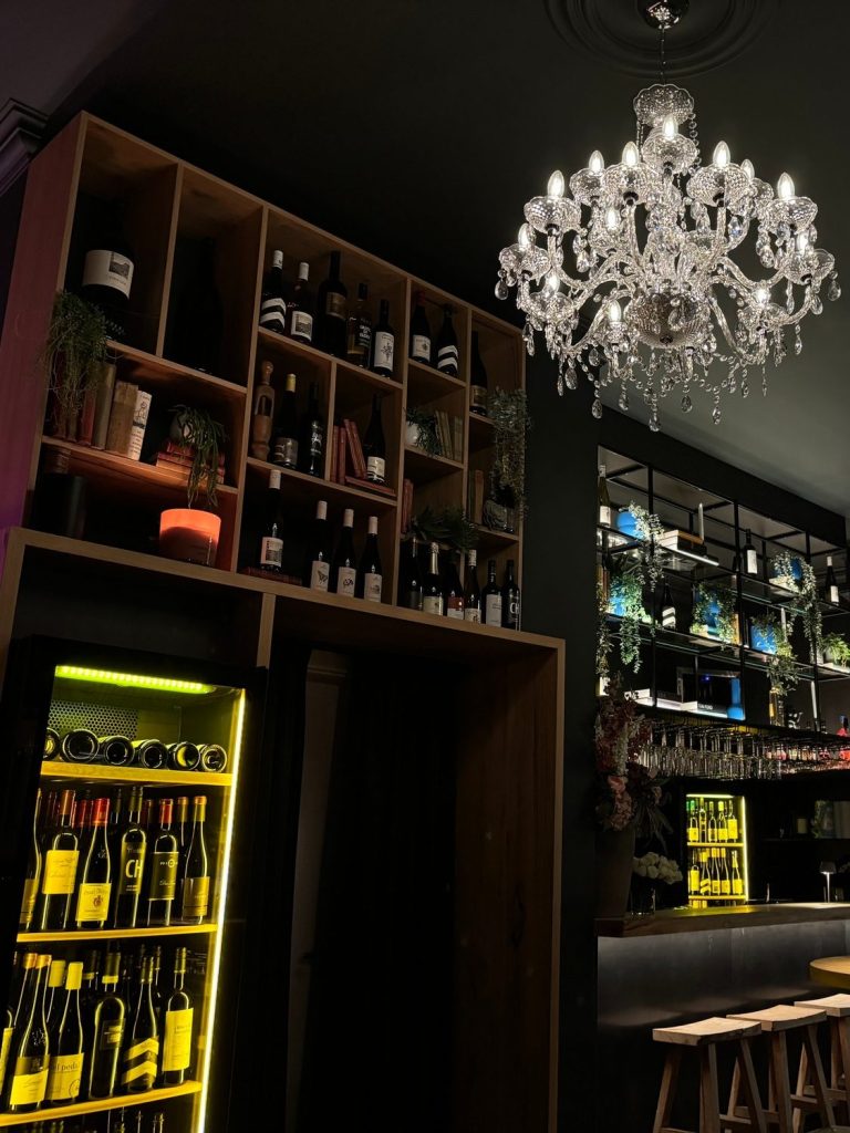 Elegante Bar Halbvoll in Kassel mit einem Kristalllüster und Regalen voller Flaschen. Dunkle, moderne Atmosphäre zum Wein trinken.