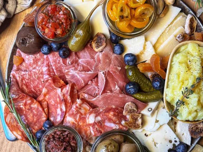 Bunte Auswahl an Wurst, Käse, Oliven, Tapenade und Früchten auf einem großen Teller.