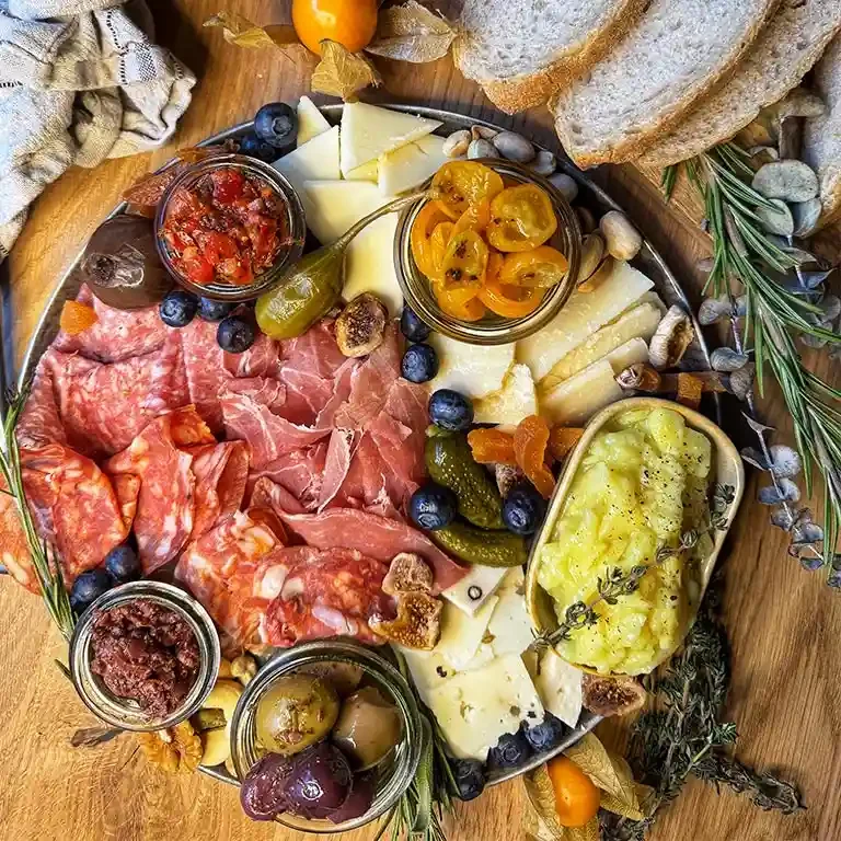 Ein Teller mit Wurst, Käse, Oliven, eingelegtem Gemüse, Trauben und Brot.
