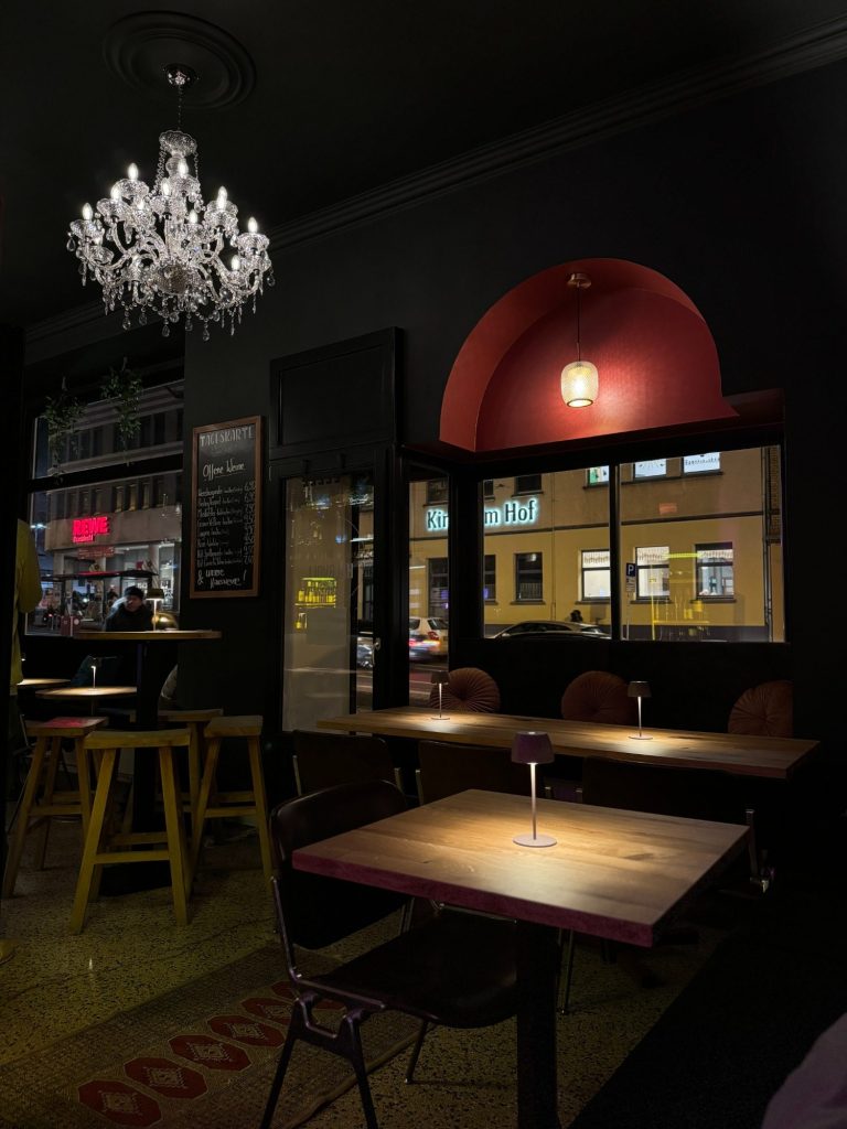 Dunkle Bar Halbvoll in Kassel mit Tisch, Stühlen und Kronleuchter, Fenster mit Blick auf die Friedrich-Ebert-Straße.